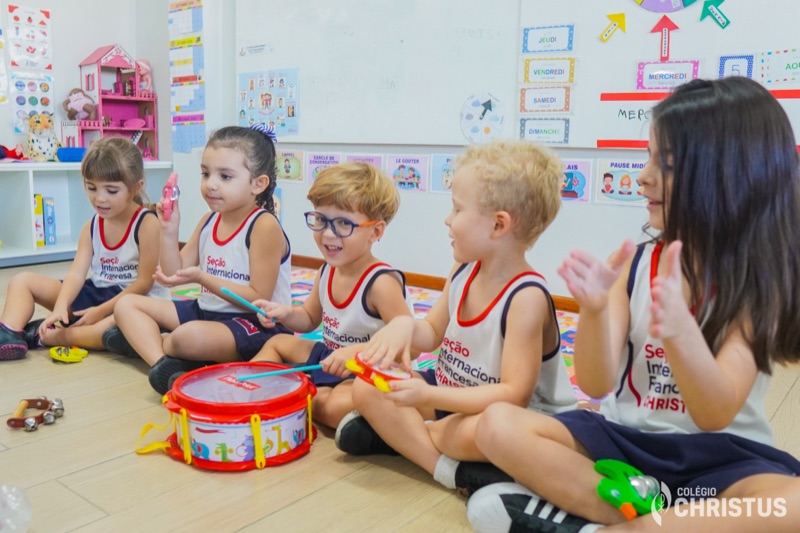 Crianças sentadas no chão tocando instrumentos na aula de musicalização